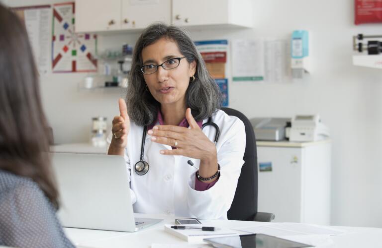 Middle-aged Latina doctor having conversation with patient in office