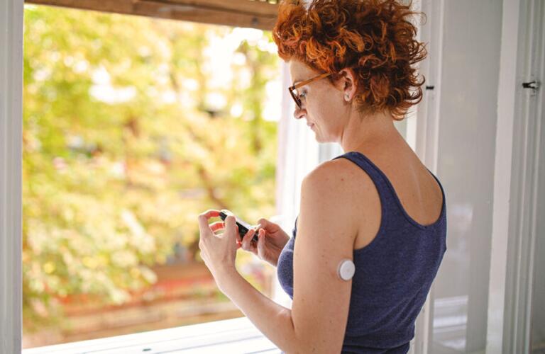 adult female wearing a patch-style blood glucose monitor