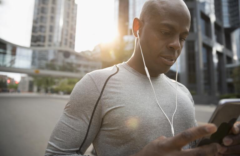 Male jogger or runner wearing headphones looking at mobile phone