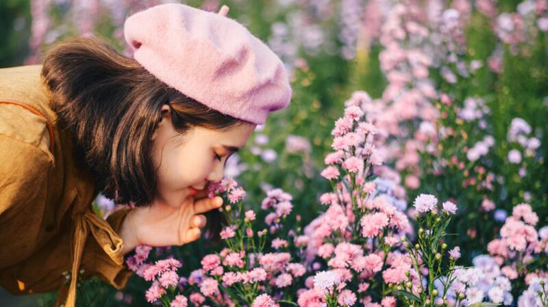 A woman leans down to smell growing flowers.
