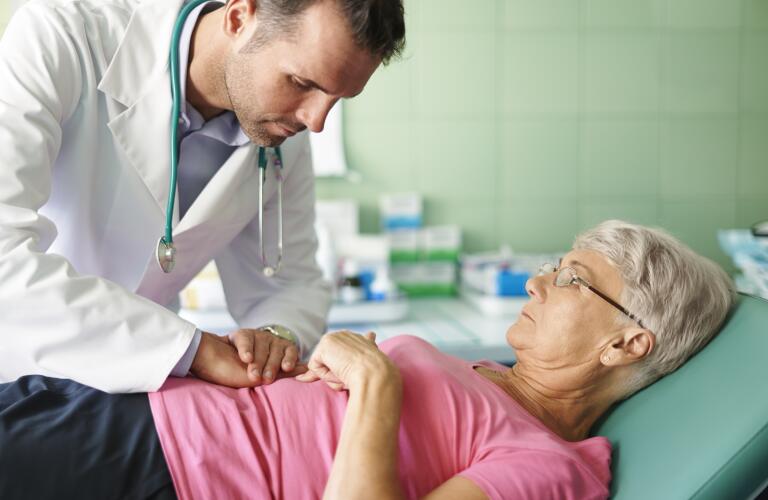 Young Caucasian male doctor examining abdomen of older Caucasian female patient