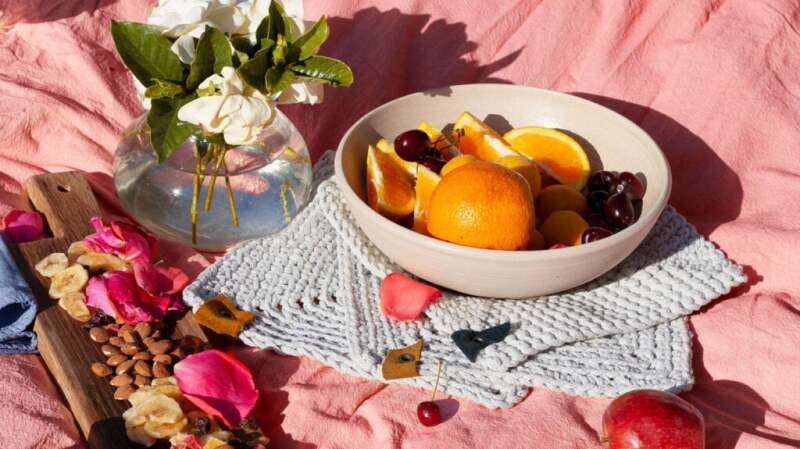 A bowel of oranges, cherries, and almonds sit on a pink blanket.