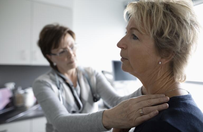 female doctor examining female patient's neck and shoulder