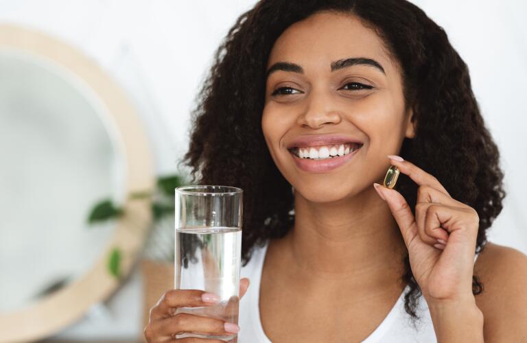 happy black woman holding omega fatty acid or vitamin D pill and water glass