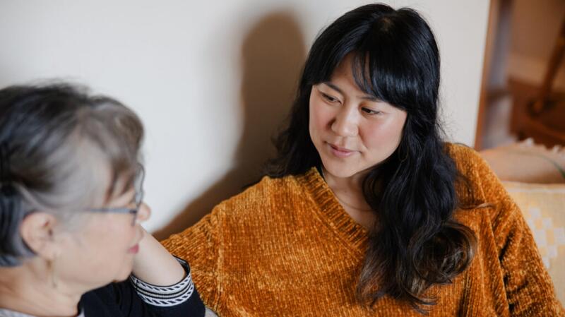 mother and daughter of East Asian descent talking while sitting on living room couch