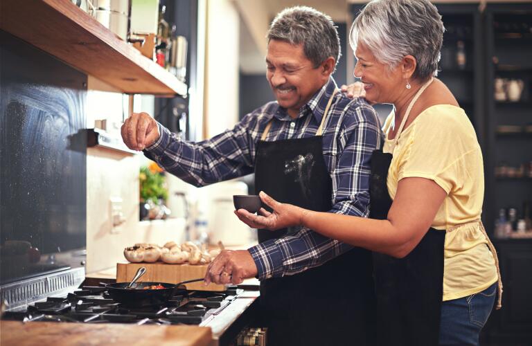 senior couple embracing and cooking in kitchen
