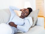 African American woman in pain on couch with hands on head and abdomen