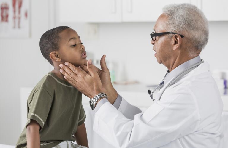 Young African American boy having throat checked by older African American doctor