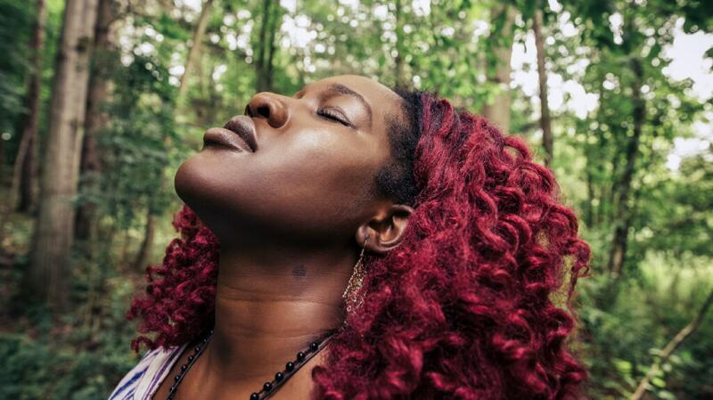 A woman closes her eyes in a forest.