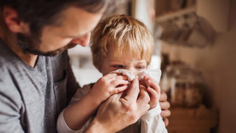 A man is helping a child blow their nose.