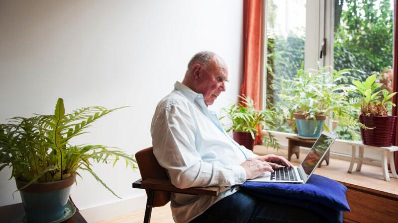 Older man sitting in a chair using a laptop