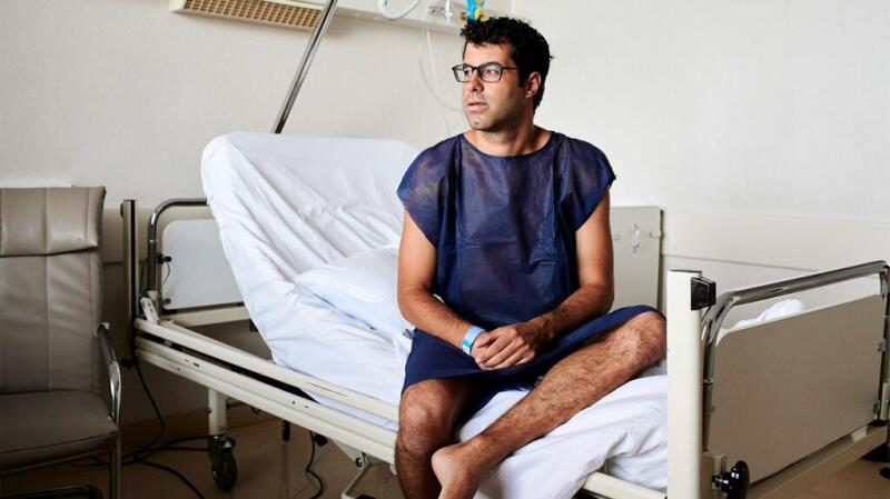 Male patient in hospital gown sitting on hospital bed