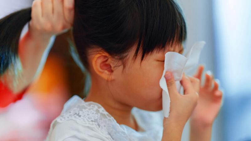 Young child blowing their nose into tissue