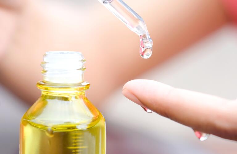 woman using dropper to apply serum or vitamin E oil on her fingertip