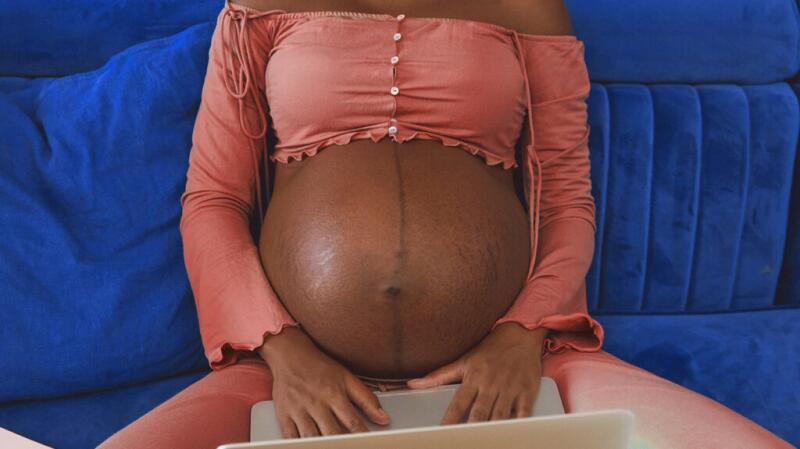 Close up of a person's pregnant stomach, sitting using a laptop