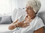 Mature Caucasian woman holding hand to chest sitting on couch