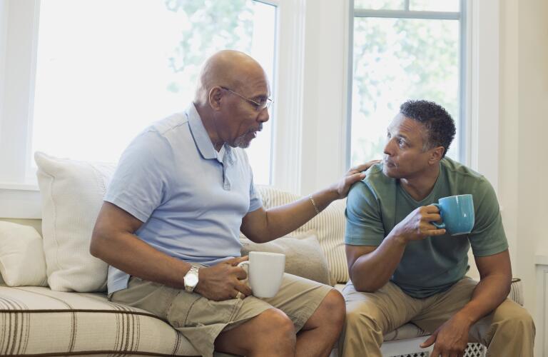 Senior father and son talking while having coffee on sofa