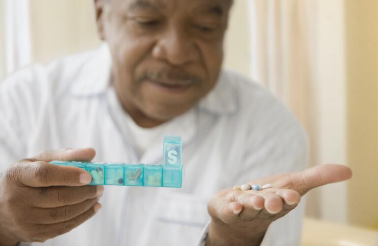 Older African American man taking pills out of weekly pill box