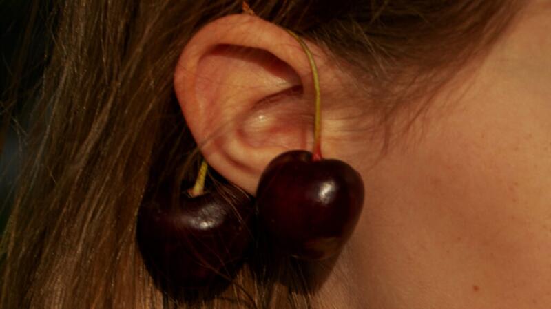 Close-up of person's ear with two cherries hung over ear