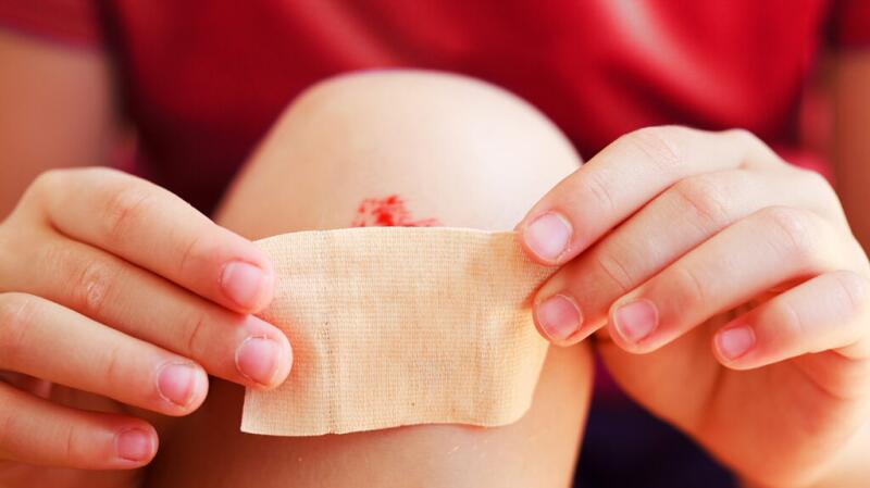 A close-up of a child putting a band-aid on their bleeding knee.