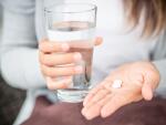 Close-up of woman's hands taking pills with glass of water