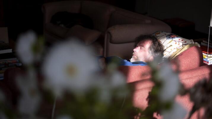 A man lies down on a sofa with his eyes closed.