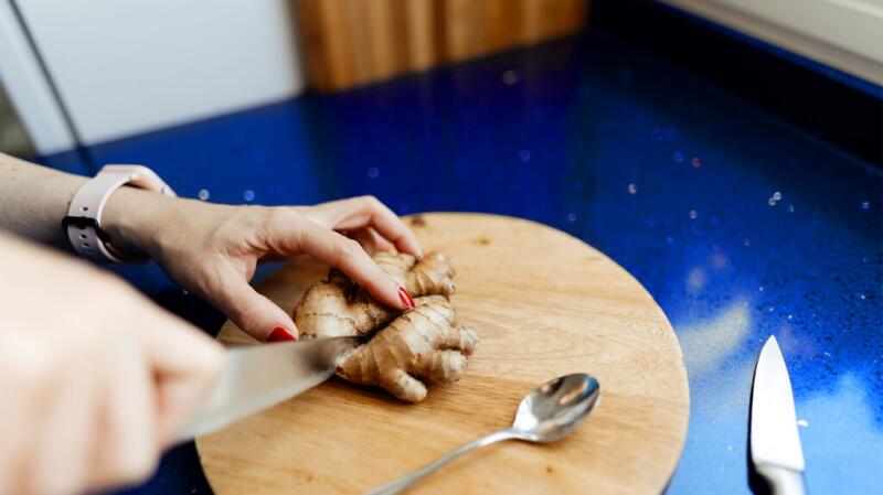 Unseen person cutting raw ginger on wood board