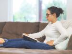 woman with stomachache, abdominal pain, or side pain sitting up on couch reading a book