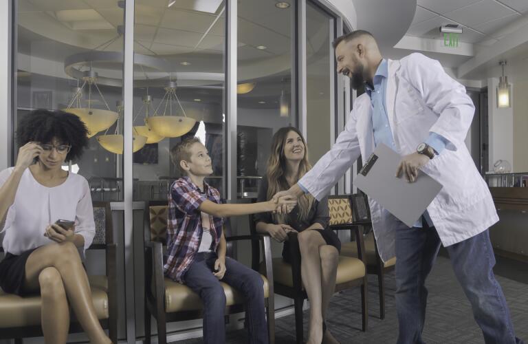 Mother with teenage son shaking doctor's hand in waiting room