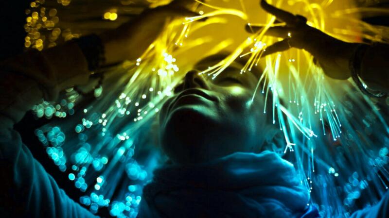 A person in a dark room is surrounded by colorful fiber-optic lights.