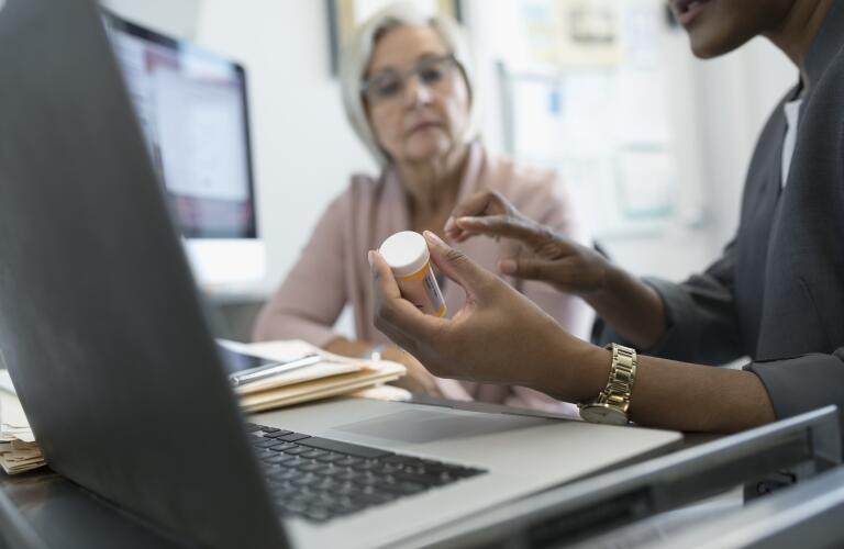 Female African American doctor showing prescription bottle to older Caucasian female patient