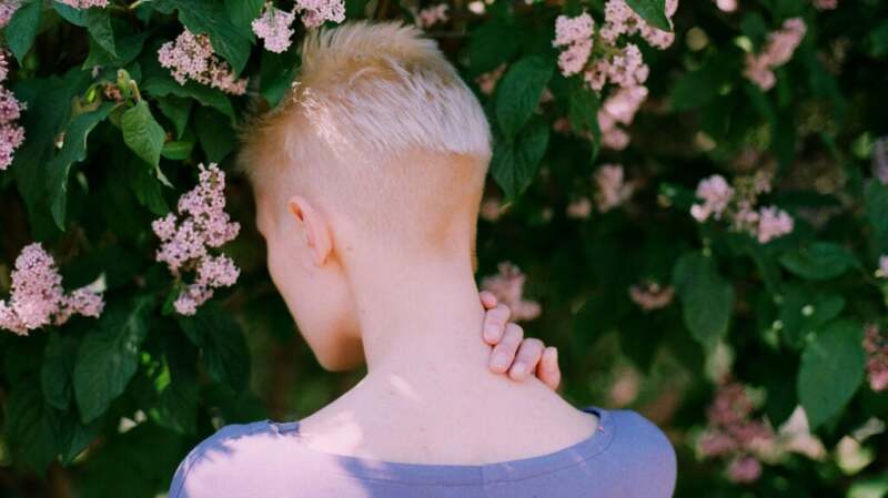 A person holds the back of their neck while standing in a garden.