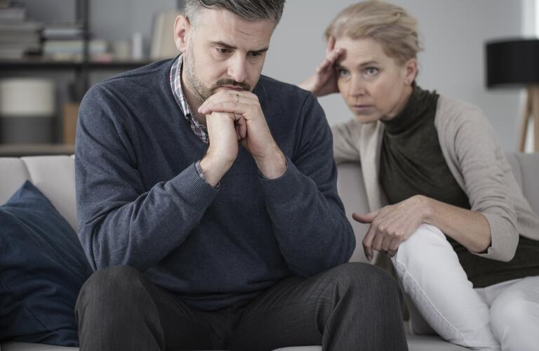 Middle aged Caucasian husband and wife on couch looking stressed and concerned