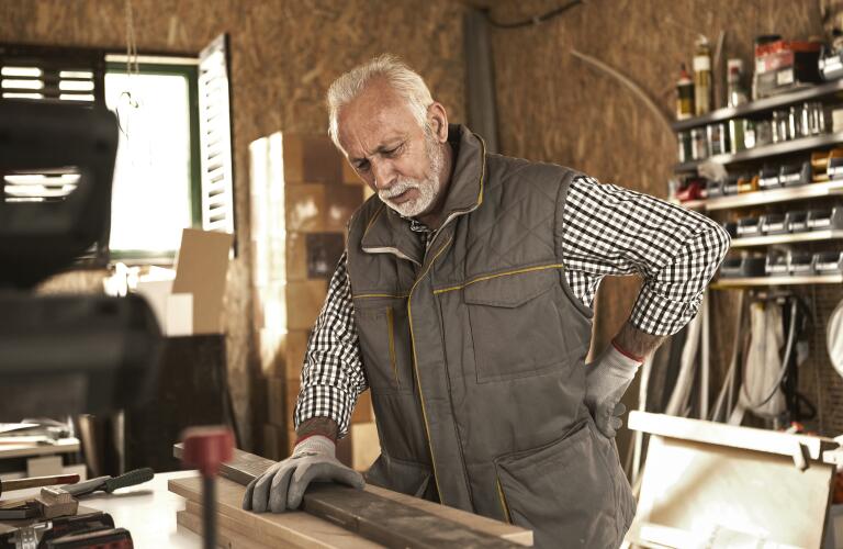 Senior man in carpentry workshop with back pain or nerve pain