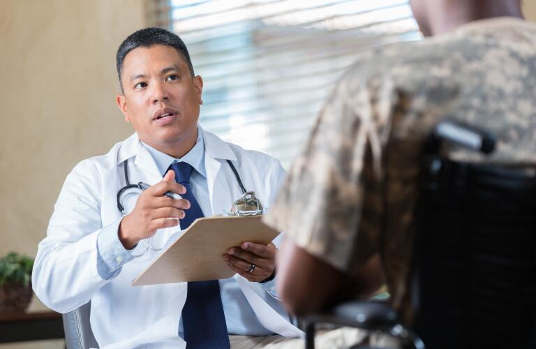 Asian American doctor talking to young African American male military veteran in wheelchair