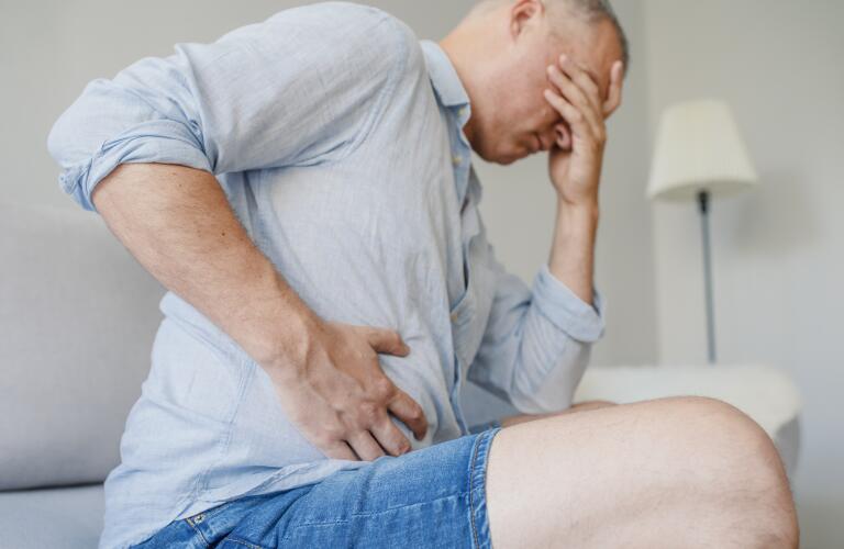 portrait of middle aged Caucasian male in pain holding side of stomach with hand over face