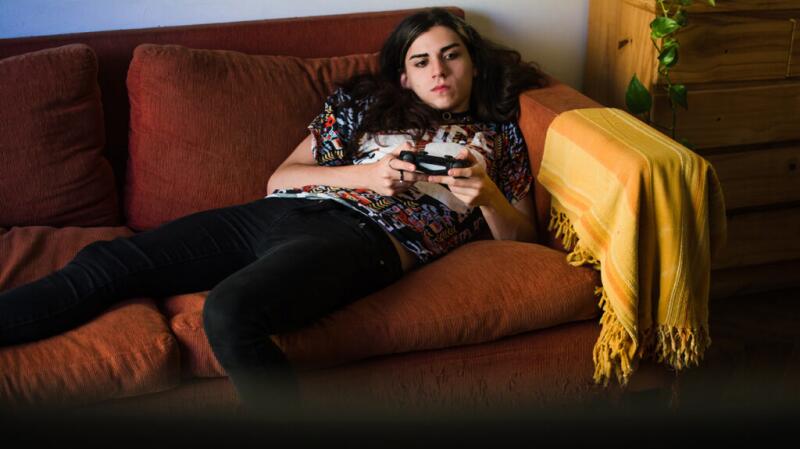 A teenager lies on a sofa while using a video game controller.