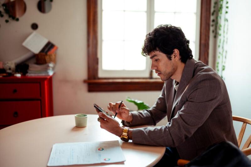 Someone sits at a table and looks at a smartphone.