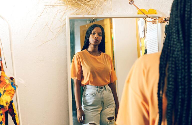 Young woman in t-shirt and jeans looking at herself in a full length mirror