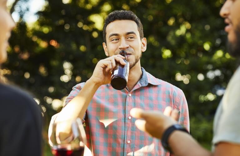 Young man drinking beer while listening to friend 