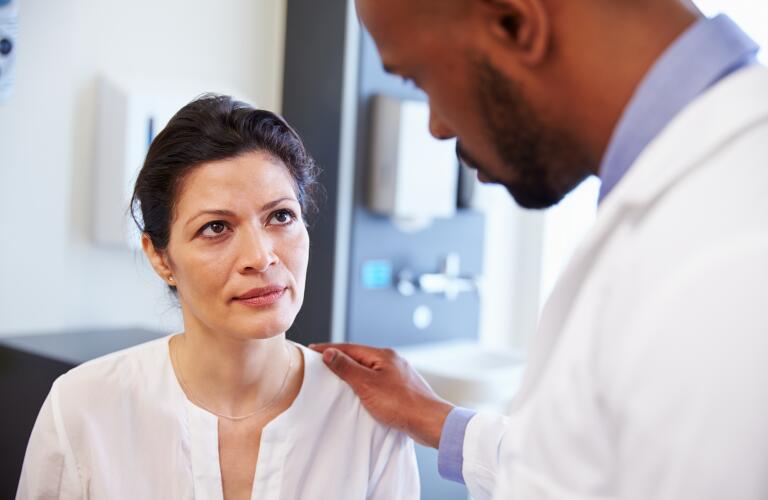 Female Patient Being Reassured By Doctor In Hospital Room